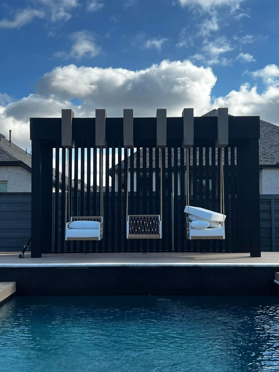 Modern slatted pergola with hanging swing seating beside a backyard pool