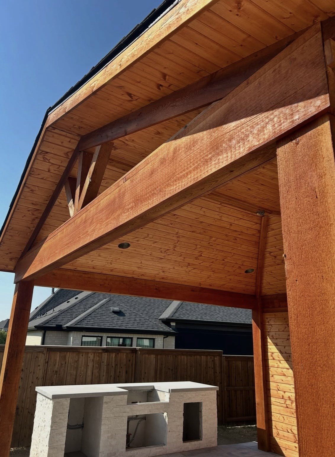 Cedar roof structure with tongue-and-groove ceiling and recessed lighting over an outdoor kitchen island mid-construction
