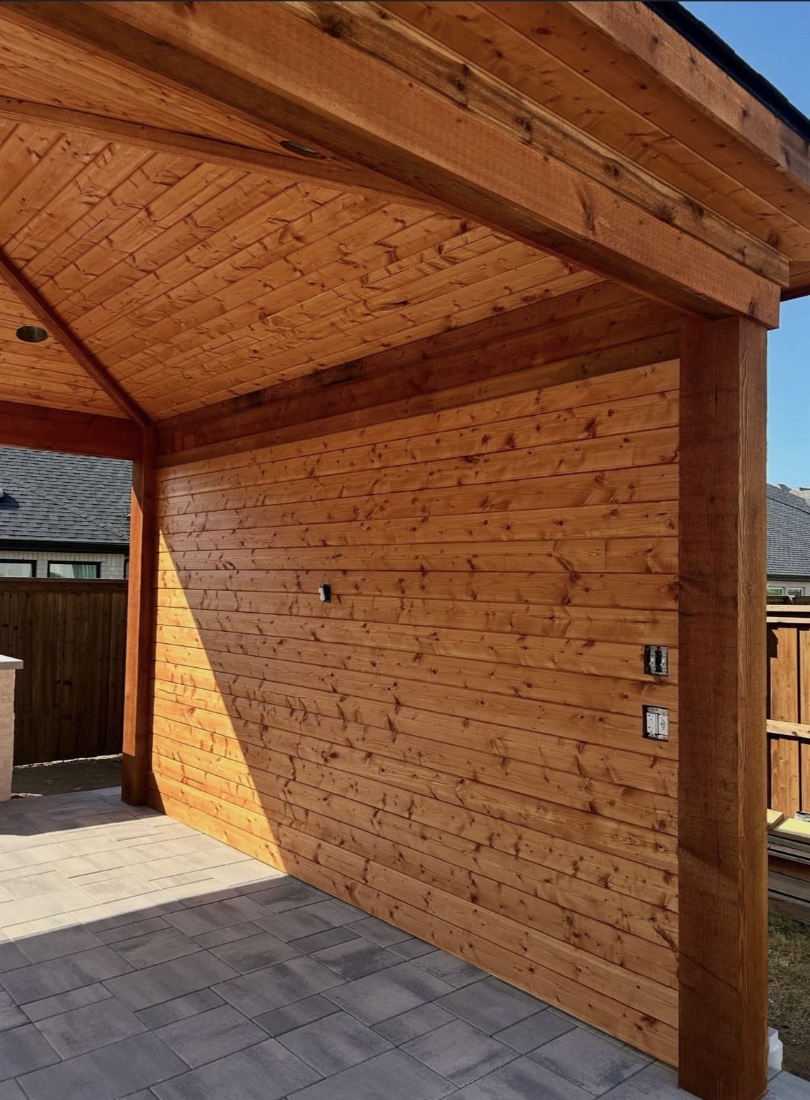 Underside of a cedar outdoor kitchen structure showing tongue-and-groove ceiling, beam, and recessed lighting