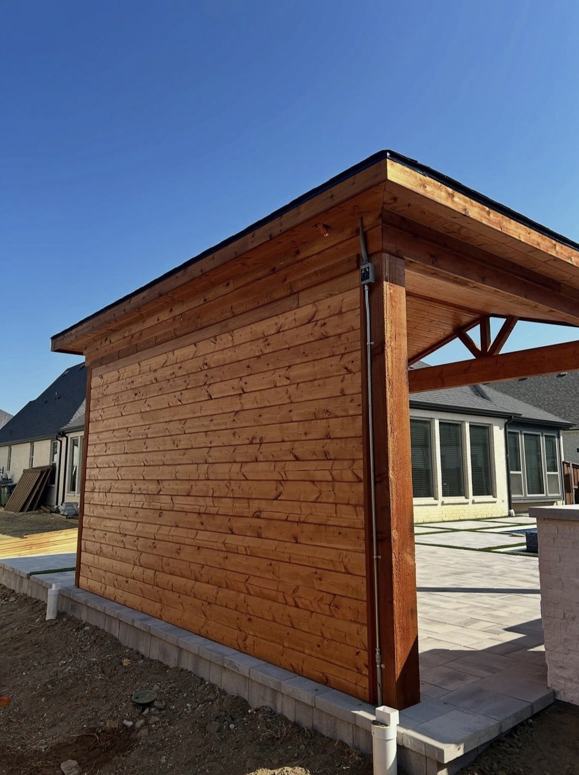 Cedar outdoor kitchen structure under construction, with the finished pool and paver patio visible beyond